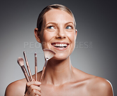 Buy stock photo Beautiful mature woman posing with makeup brush in studio against a grey background