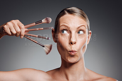 Buy stock photo Beautiful mature woman posing with makeup brush in studio against a grey background