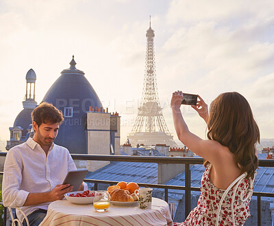 Buy stock photo Romantic, holiday and couple at cafe with Eiffel Tower, phone and photography of city architecture. Man, woman and digital memory on vacation in evening with skyline of Paris on restaurant balcony