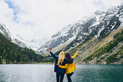 Buy stock photo Women, friends and open arms in lake on mountain with snow for winter holiday and adventure. Back view, tourist and freedom in water dam at countryside for hiking, camping and bonding in Canada