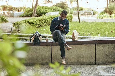 Black businessman writing in a notebook while sitting in a park. Taking a lunch break from the office to do some planning in his diary