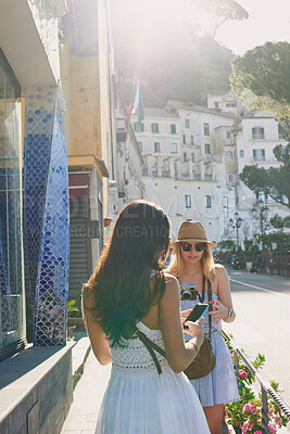 Buy stock photo Shot of an attractive young woman standing with her friend and using their cellphones during their holiday in Italy