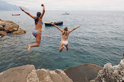 Buy stock photo Full length shot of two unrecognisable women jumping into the Mediterranean Sea during their holiday in Italy