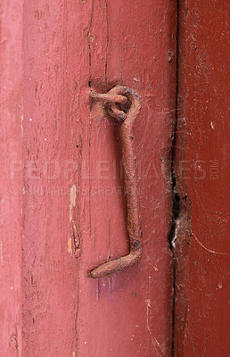 Buy stock photo Closeup of textured red door with a rusty metal hook. Bright wooden doorway and doorframe aged with cracked patterns, scuff marks and chipped wood. Exterior view of entrance to old and worn woodshed