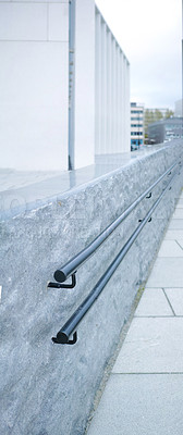 Buy stock photo Closeup of metal railing alongside a grey stone wall in the city. Macro view of handrails downtown with urban buildings in the background. Balance and stability for a morning commute into town