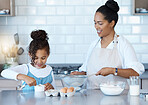 Happy young mixed race woman enjoying baking with her little daughter in the kitchen at home. Little hispanic girl smiling while helping her mother cook a meal at home