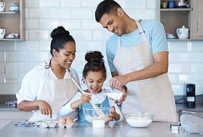 Happy young carefree mixed race family cooking together in the kitchen at home. Little cheerful hispanic girl smiling while helping her parents bake a snack in the kitchen at home