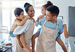Energetic parents giving their children a piggyback ride while wearing aprons and baking in the kitchen. Hispanic mom and dad playing with kids at home