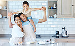 Portrait of happy young mixed race couple bonding with their adorable son in a home kitchen while baking. Hispanic husband carrying a child on his shoulders while his wife embraces him. Time together