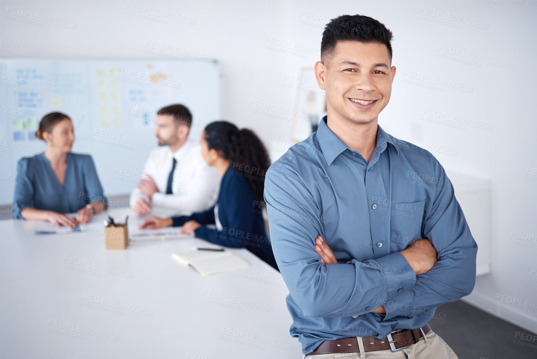 Buy stock photo Portrait of confident smiling mixed race businessman leaning on desk in a boardroom with arms folded. Diverse group of businesspeople in meeting and working behind happy hispanic manager in an office