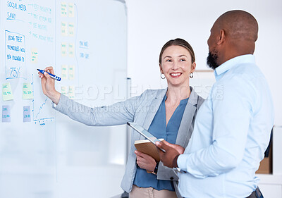 Team of smiling business people using whiteboard to brainstorm strategy in office. Caucasian businesswoman standing with african american businessman and writing while planning. Two happy colleagues