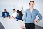 Portrait of confident smiling caucasian businesswoman leaning on a desk in aa boardroom. Diverse group of businesspeople in a meeting and working behind a happy young business manager in an office