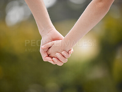 Closeup of a mother holding her child\'s hand while walking outside against greenery on a sunny day. A parent will guide, protect and keep family safe