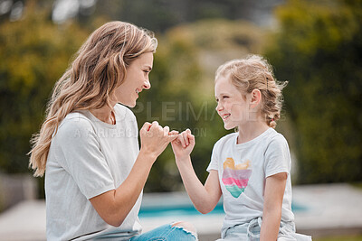 Happy young caucasian mother sitting with her adorable little daughter in the garden at home and making pinky promises. Cute little girl bonding with her parent in the backyard swearing to secrecy