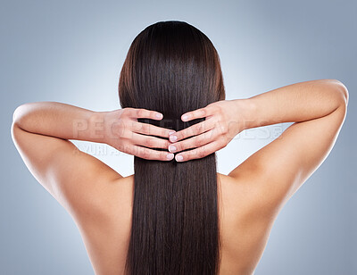 Rear view of a woman touching her beautiful smooth and shiny hair. Mixed race brunette woman with luxurious straight and healthy long brown hair against a studio background