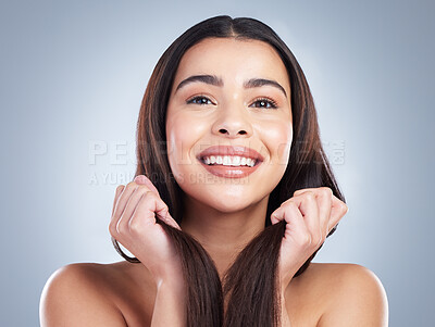 Portrait of a beautiful mixed race woman with clean skin and shiny smooth hair posing against a studio background. Woman holding her hair to show off healthy hair care