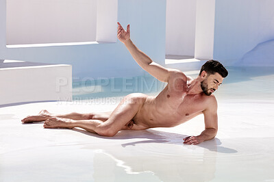 One handsome nude caucasian man posing naked like a greek god while lying outside in a pool of water. Sexy young male model looking sensual and seductive while flaunting muscular body in nude