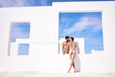 Two nude muscular caucasian men kissing passionately outdoors against a white artistic structure and blue sky. Young homosexual couple in love exposing naked body and sharing intimate moment together