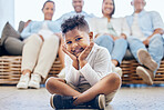 Portrait of adorable african american boy sitting with his legs crossed on the floor while family sits on chair in the background. Cute little boy smiling while sitting at home