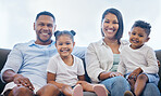 Happy mixed race family of four smiling while relaxing on a sofa together at home. Carefree loving parents bonding with two cute little kids. Adorable young girl and boy relaxing with mom and dad