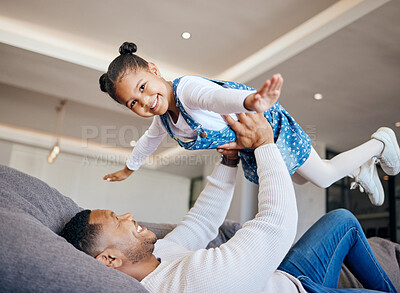 Adorable little girl being lifted in the air by her dad. Excited little girl having fun and playing with her father at home. Mixed race family having fun on the couch at home