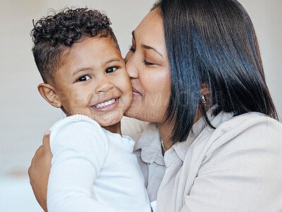 Mixed race woman kissing her adorable little son on the cheek while bonding together at home. Small hispanic boy smiling and looking happy to be getting love and affection from his mom