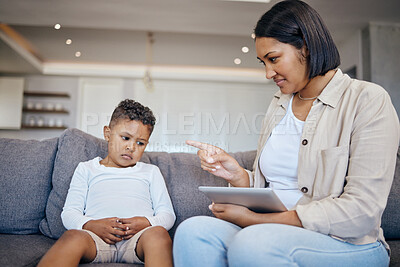 Mixed race woman pointing to scold and discipline her little son about internet use on digital tablet at home. Naughty boy looking sad while mother punishes him for playing too many games online