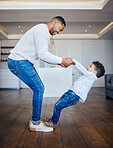 Little boy standing on dad's feet and sharing a dance. Playful dad and son having fun together at home. Cheerful man teaching his son to dance