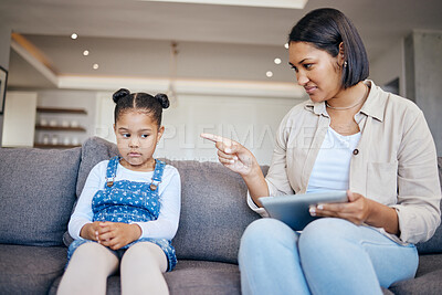 Mixed race woman pointing to scold and discipline her little daughter about internet use on digital tablet at home. naughty girl looking sad while mother punishes her for playing too many games online