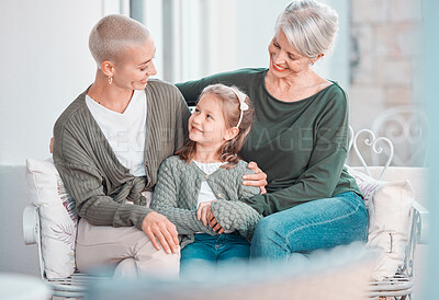 Three generations of females sitting together and looking at each other. Adorable little girl bonding with her mother and grandmother at home