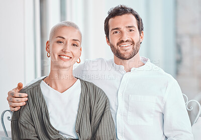 Portrait of happy young caucasian couple posing together seated on a chair in their home. Man sitting with his arm around his wife. Happy and healthy marriage