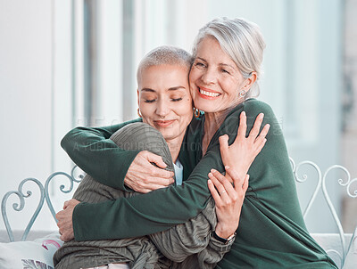 Cheerful senior mother hugging her adult daughter. Loving caucasian mom giving her daughter a hug while sitting on a chair together at home. Content woman bonding with her mother during a visit