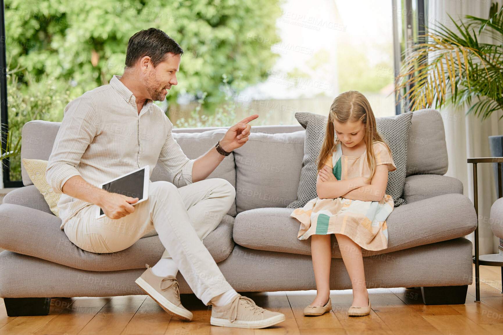 Buy stock photo Parent, child and tablet with discipline on a sofa in the living room for naughty behavior at home. Upset, angry and young strict dad talking to sad girl kid on the couch in lounge at modern house.