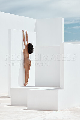 Beautiful mixed race woman modelling naked while climbing and hanging with her body pressed up a white wall. One sexy female looking sensual, erotic and seductive while flaunting her hot slim body