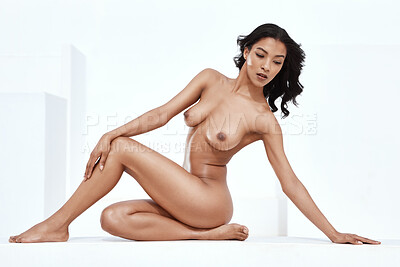 Beautiful mixed race woman sitting alone outside against a white background and posing nude. Sexy hot hispanic model showing naked body and breasts. Nudist feeling sensual, seductive, touching her leg