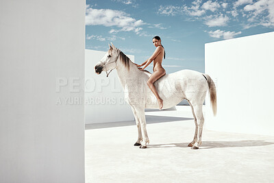 Fullbody of beautiful mixed race woman posing nude while sitting on a horse outside. Sexy hot hispanic model showing her naked body on white stallion. Nudist feeling sensual, seductive, free on a mare
