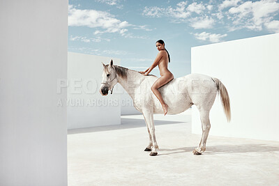 Portrait full body of beautiful mixed race woman posing nude while sitting on a white horse outside. Alluring hispanic model showing her naked body on white stallion. Nudist sensual, seductive, free
