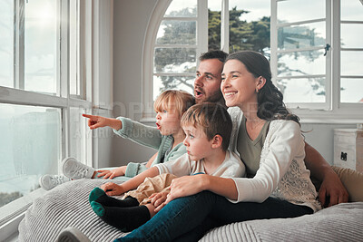 Buy stock photo Young caucasian couple enjoying the view from a window while bonding with their adorable little children on a comfy seat. Cute kid looking amazed and pointing in surprise while sitting with her family