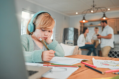 Closeup of a cute caucasian little brunette girl wearing wireless headphones while holding a pencil and being creative by drawing in a book at home with her parents and brother in the background. Young girl listening to music with her wireless device with