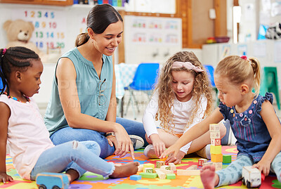 Teacher and kids looking happy while doing activity at kindergarten or pre-school. Smiling teacher sitting on a colourful mat with diverse group of toddlers while playing with building blocks