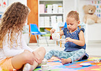 Two little girls having a tea party while playing on a colourful mat on the floor at preschool or kindergarten. Happy caucasian kids engaged in fun creative imaginative learning and development