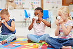 A group of diverse little girls having a tea party while playing on a colourful mat on the floor at preschool or kindergarten. Mixed race children having fun while being creative and playing 