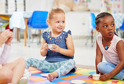 Little girls having a tea party while playing on a colourful mat on the floor at preschool or kindergarten. Happy diverse kids having fun while engaged in creative imaginative learning and development