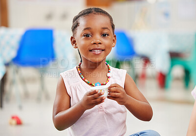 Portrait of one adorable little african american cute girl sitting alone in preschool and holding a small teacup. Smiling adorable child playing and having a tea party at school. Social skills develop children at creche