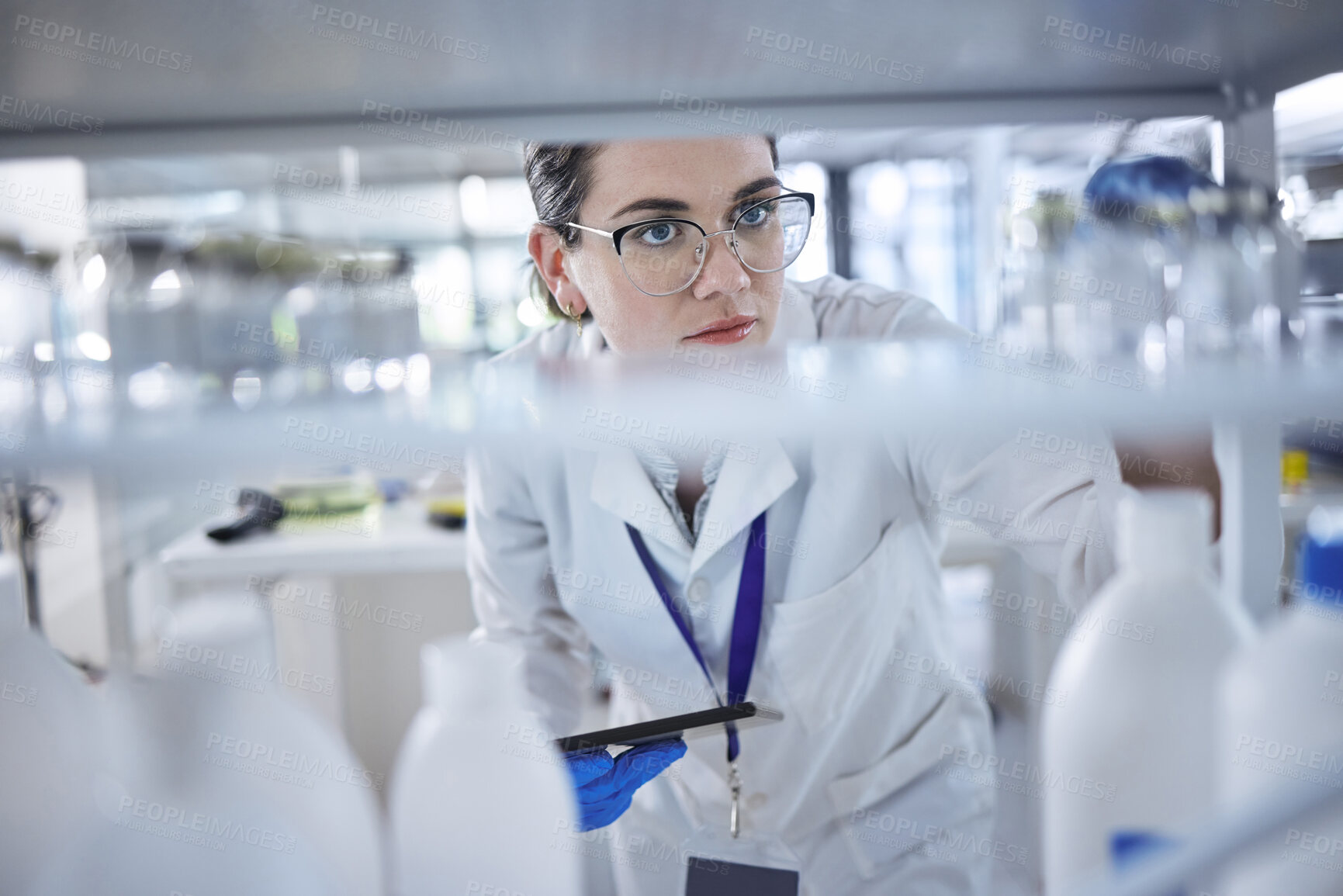 Buy stock photo One caucasian medical scientist wearing glasses and looking at a medicine vial in a laboratory. Healthcare pathologist discovering a cure in a clinic. Control diseases with science and a digital tablet
