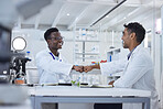 Two smiling medical scientists sitting together in a laboratory and fist bumping. African American and mixed race healthcare professionals celebrating a success. Teamwork and unity in curing diseases