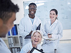 Diverse team of young doctors laughing in lab coats discussing work in laboratory
