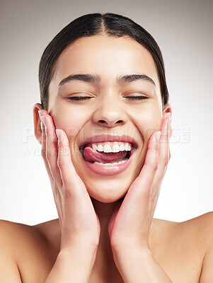 Young joyful mixed race woman touching and feeling her face while sticking out her tongue and posing against a grey studio background. Confident hispanic female smiling while posing against a background