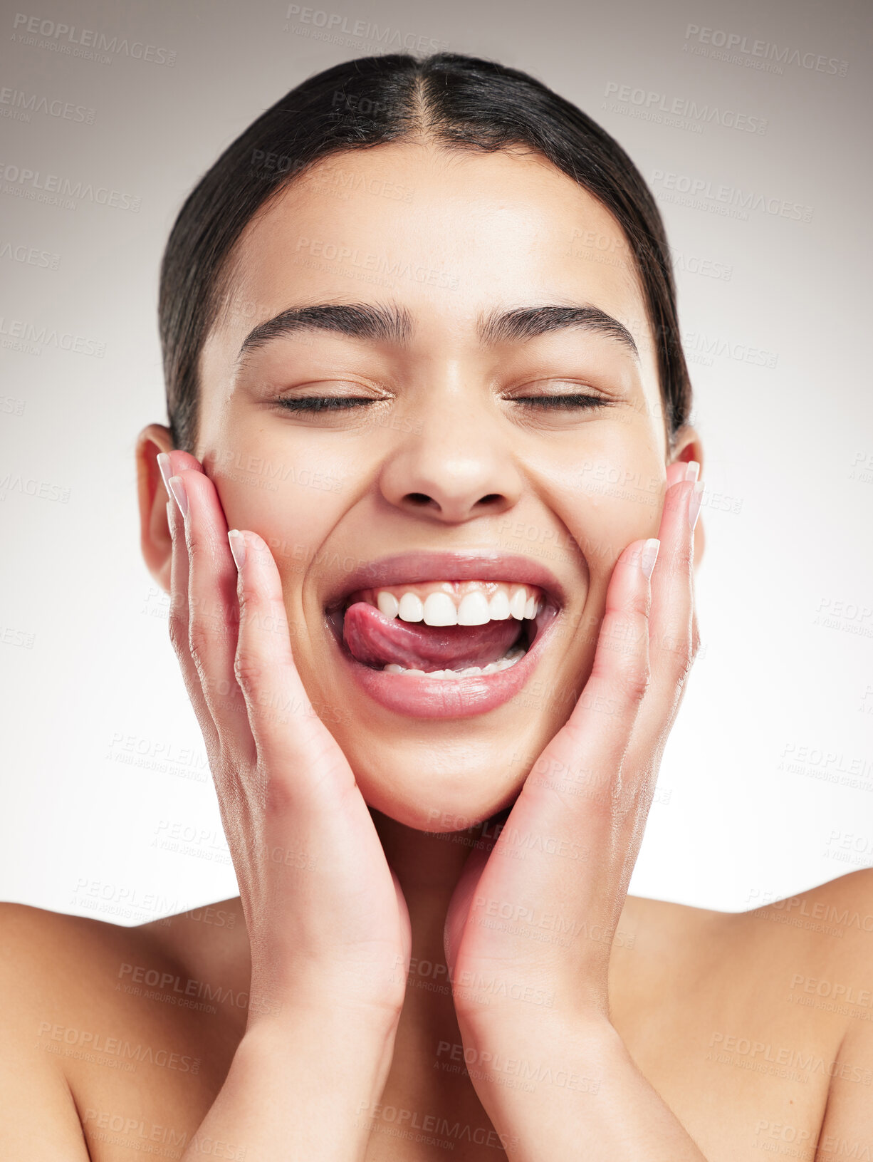 Buy stock photo Young joyful mixed race woman touching and feeling her face while sticking out her tongue and posing against a grey studio background. Confident hispanic female smiling while posing against a background