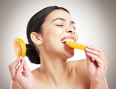 Buy stock photo Young beautiful mixed race woman eating an orange while posing against a grey background. One cheerful hispanic female eating a healthy fruit against a background